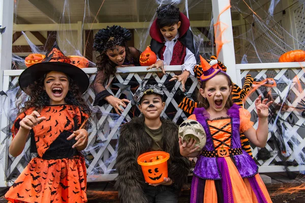 Meninas em trajes de Halloween sorrindo para a câmera perto de amigos multiétnicos ao ar livre — Fotografia de Stock