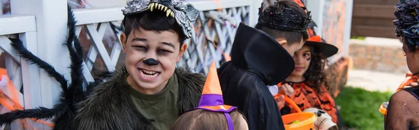 Preteen asiático menino no halloween traje sorrindo perto amigos durante festa ao ar livre, banner — Fotografia de Stock