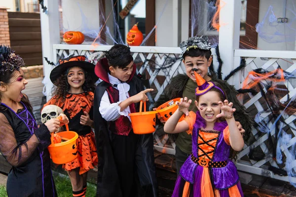 Interracial kids in halloween costumes holding buckets and playing outdoors — Stock Photo