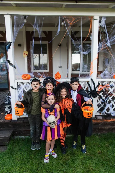 Preteen amigos multiétnicos sorrindo para a câmera durante a celebração halloween no quintal da casa — Fotografia de Stock