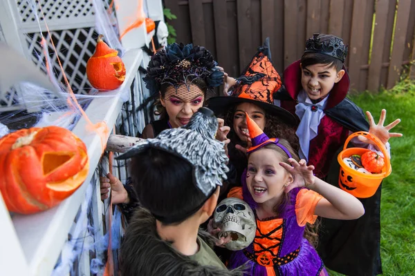 Високий кут зору багатоетнічних дітей лякає друга під час святкування Хеллоуїна на задньому дворі — стокове фото