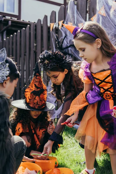 Multiethnic kids in costumes taking candies from buckets during halloween celebration outdoors — Stock Photo