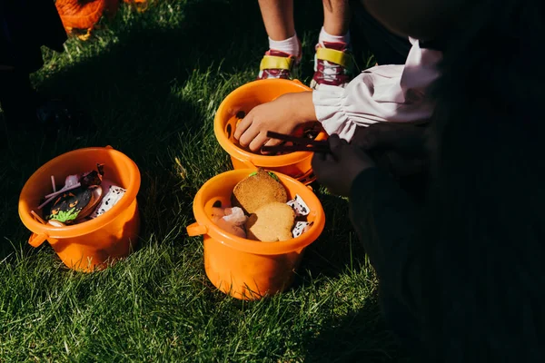 Vista recortada del niño tomando caramelos del cubo durante la fiesta de halloween al aire libre - foto de stock