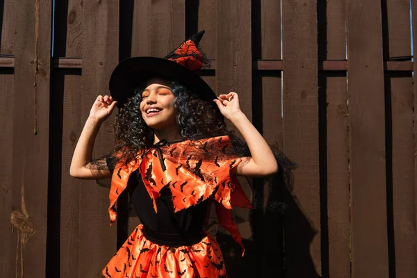 Положительный ребенок держит шляпу ведьмы во время празднования Хэллоуина на открытом воздухе — стоковое фото