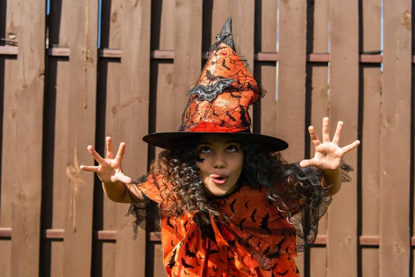 Spooky preteen kid in halloween costume and with hat grimacing outdoors — Stock Photo