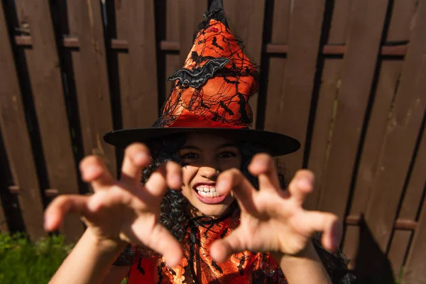 Alto ángulo vista de niño en halloween bruja sombrero mueca en la cámara al aire libre - foto de stock