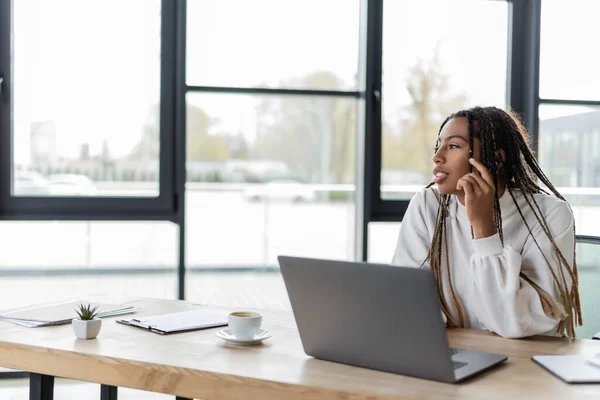 Африканская американская деловая женщина смотрит в сторону возле кофе и ноутбука в офисе — стоковое фото