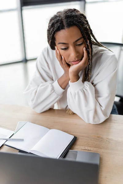 Femme d'affaires afro-américaine à la recherche d'un ordinateur portable près d'un ordinateur portable avec espace de copie dans le bureau — Photo de stock