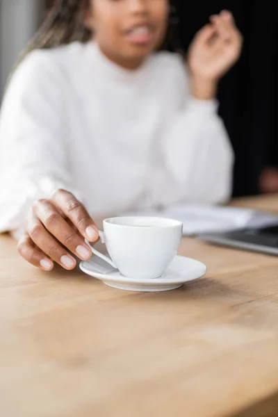 Cropped view of blurred african american businesswoman taking cup of coffee in office — Stock Photo