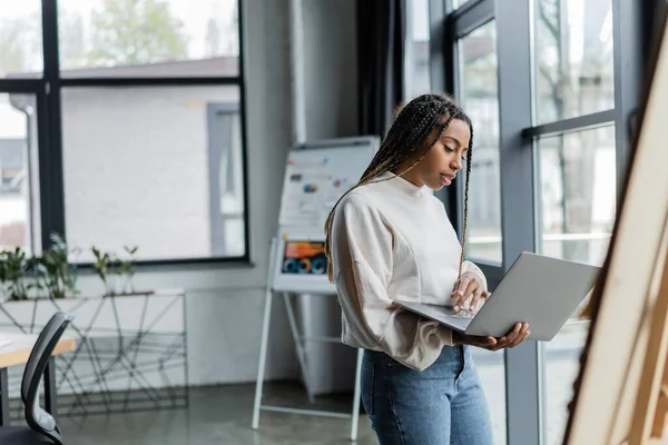 Empresaria afroamericana en ropa casual usando laptop en oficina moderna - foto de stock