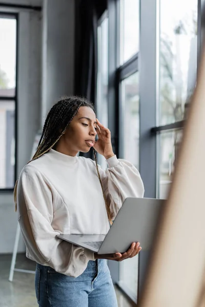 Focused african american businesswoman in sweatshirt holding laptop in office — Stock Photo