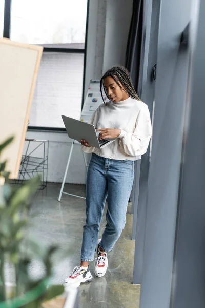 Empresária afro-americana em roupas casuais usando laptop no escritório moderno — Fotografia de Stock