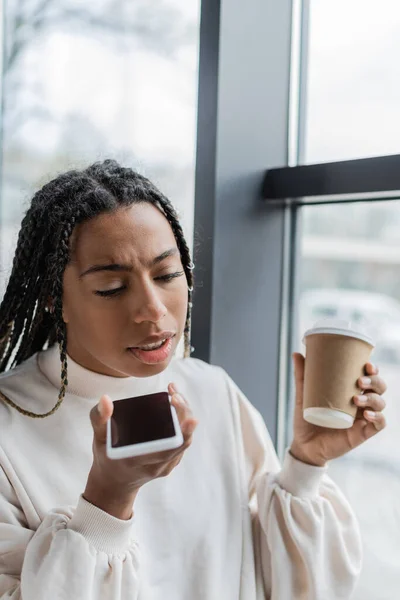Africano americano empresária gravação mensagem de voz no smartphone e segurando café para ir — Fotografia de Stock
