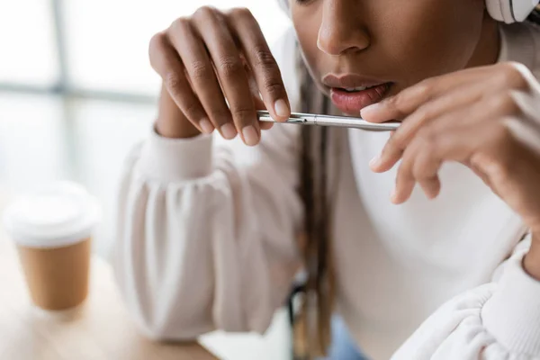 Vista cortada da mulher de negócios americana africana segurando caneta perto de café borrado para ir no escritório — Fotografia de Stock