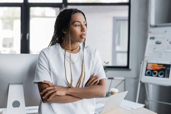 African american businesswoman in t-shirt looking away near devices on table in office — Stock Photo