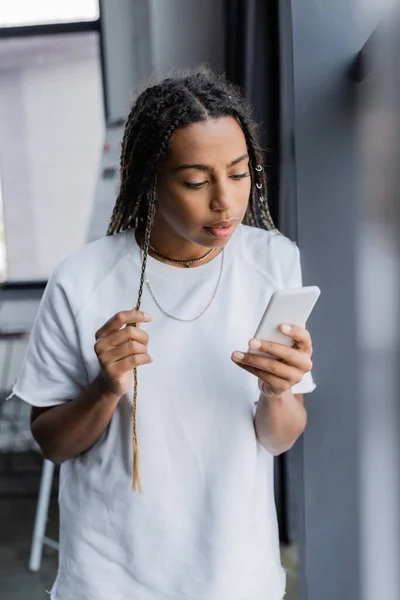 Empresaria afroamericana en camiseta usando smartphone en oficina borrosa - foto de stock