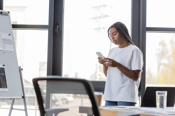 Femme d'affaires afro-américaine en vêtements décontractés en utilisant un smartphone au bureau — Photo de stock