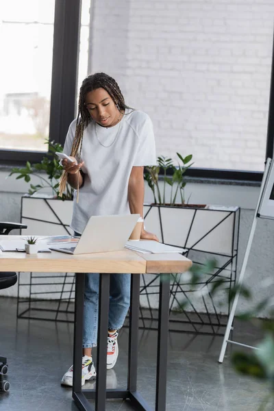 Gestionnaire afro-américain en vêtements décontractés en utilisant des gadgets près des papiers dans le bureau moderne — Photo de stock