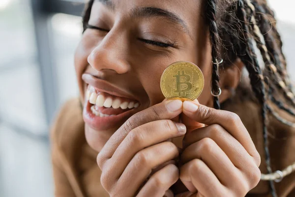 KYIV, UCRAINA - APRILE 27, 2022: Positiva donna d'affari afroamericana in possesso di bitcoin d'oro in carica — Foto stock