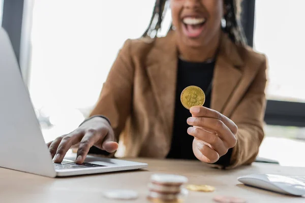 KYIV, UKRAINE - APRIL 27, 2022: Cropped view of blurred african american businesswoman holding bitcoin near laptop in office — Stock Photo