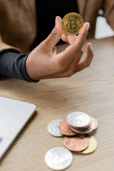 KYIV, UKRAINE - 27 avril 2022 : Vue recadrée d'une femme d'affaires afro-américaine tenant crypto-monnaie près d'un ordinateur portable au bureau — Photo de stock