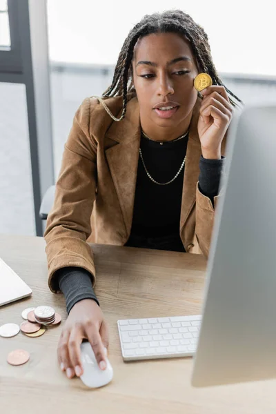 QUIIV, UCRÂNIA - 27 de abril de 2022: Empresária afro-americana segurando bitcoin e usando computador no escritório — Fotografia de Stock