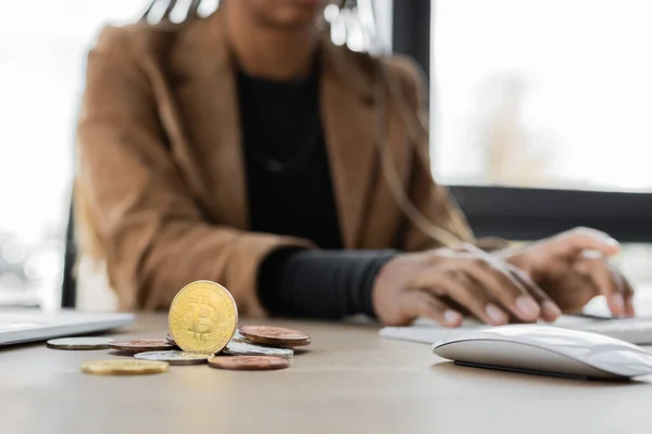 QUIIV, UCRÂNIA - 27 de abril de 2022: Vista cortada de bitcoins perto de mulher de negócios afro-americana borrada digitando no teclado do computador — Fotografia de Stock