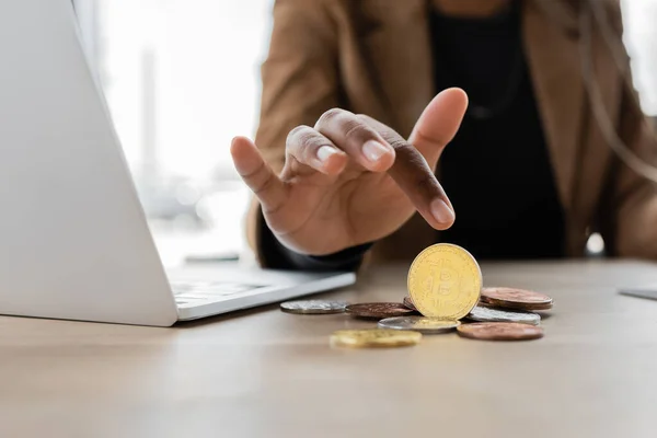 KYIV, UKRAINE - APRIL 27, 2022: cropped view of african american businesswoman pointing at bitcoins near laptop in office — Stock Photo