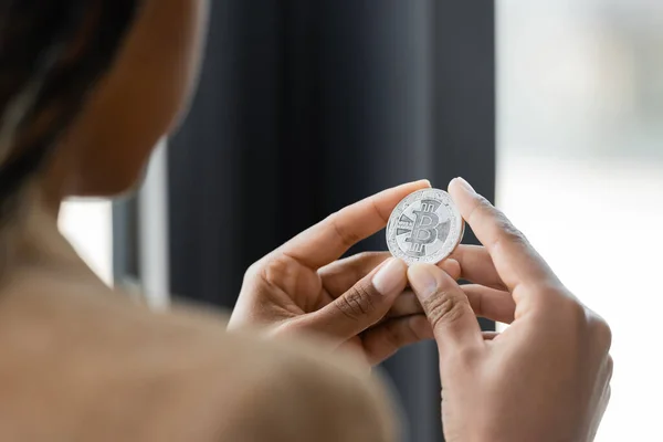 KYIV, UKRAINE - APRIL 27, 2022: Cropped view of blurred african american businesswoman holding silver bitcoin in office — Stock Photo