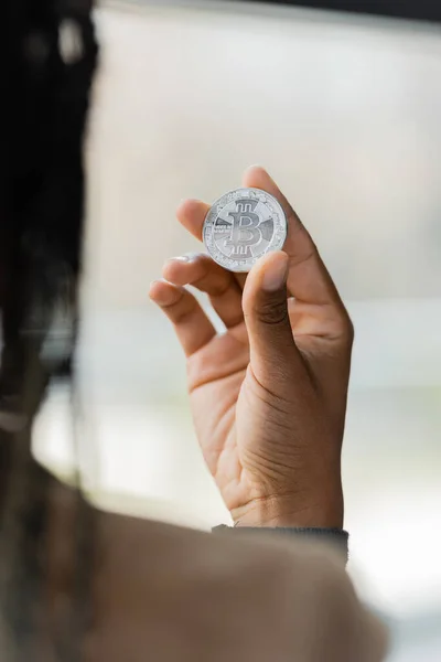 KYIV, UKRAINE - APRIL 27, 2022: Blurred african american businesswoman holding silver bitcoin in office — Stock Photo