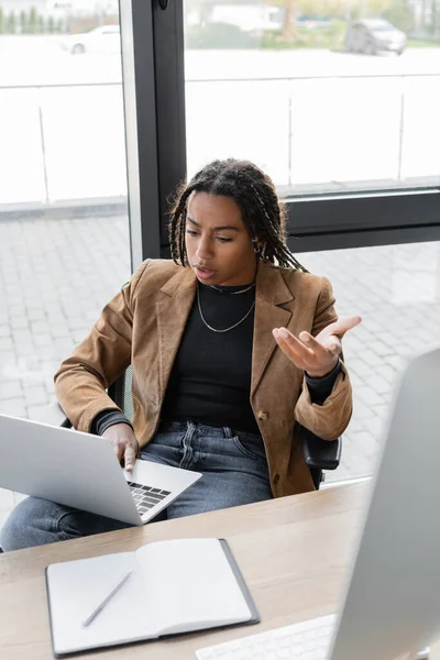 African american businesswoman having video call on laptop near notebook on table in office — Stock Photo