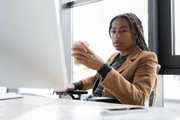 Donna d'affari afroamericana che tiene il caffè per avvicinarsi al computer in ufficio — Foto stock