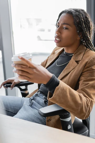 African american businesswoman in jacket holding coffee to go in office — Stock Photo