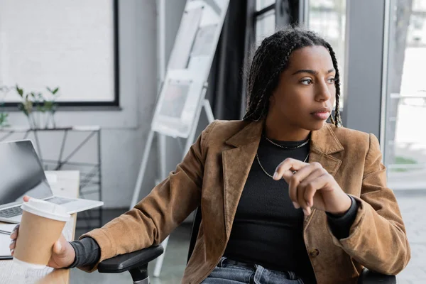 African american businesswoman in jacket holding coffee to go in office — Stock Photo