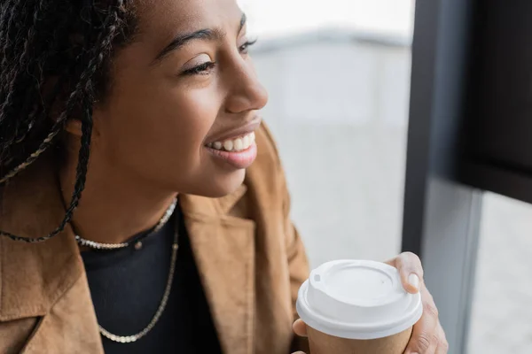 Smiling african american businesswoman in jacket holding paper cup in office — Stock Photo