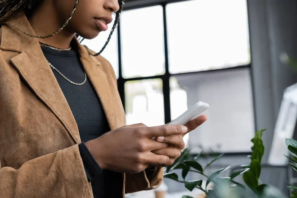 Vue recadrée d'une femme d'affaires afro-américaine en blazer à l'aide d'un téléphone portable au bureau — Photo de stock