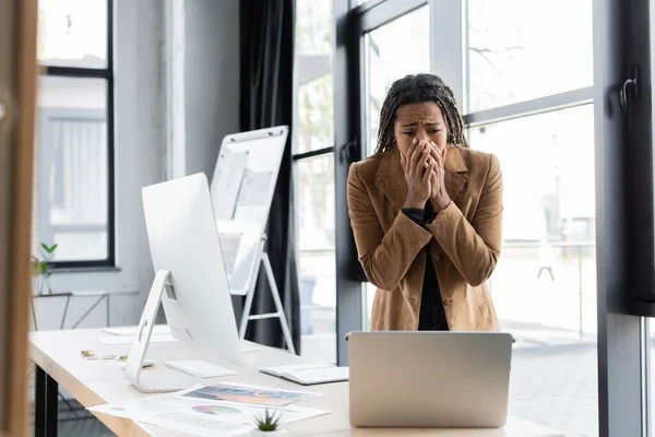 Стрес афроамериканського бізнесмена, який дивиться на ноутбук біля документів у офісі — стокове фото