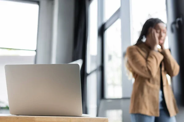 Laptop on table near blurred african american businesswoman in office — Stock Photo