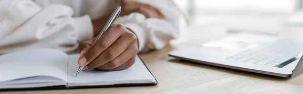 Vista cortada da mulher de negócios afro-americana escrevendo no notebook perto do laptop na mesa, banner — Fotografia de Stock