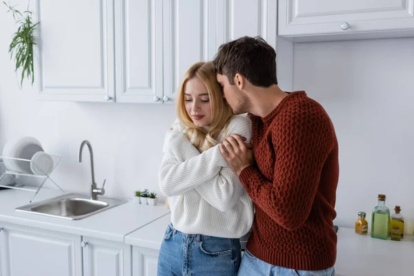 Молодой человек в красном свитере обнимает чувственную блондинку на кухне — стоковое фото