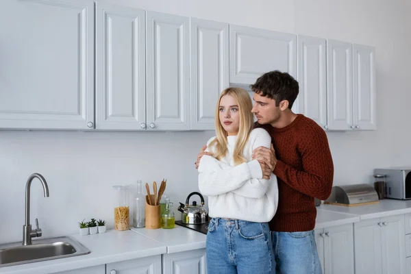 Мужчина в трикотажном свитере обнимает блондинку на белой кухне — стоковое фото