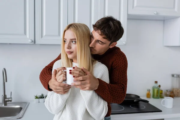 Junger Mann im roten Pullover umarmt blonde Frau im Winter mit einer Tasse Tee — Stockfoto