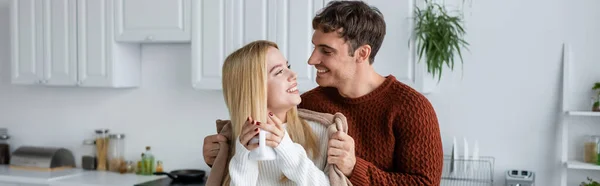 Caring man holding blanket near happy girlfriend in sweater with cup of tea, banner — Stock Photo