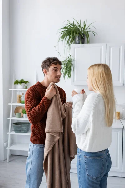 Jeune homme tenant couverture près de petite amie en pull avec tasse de thé — Photo de stock