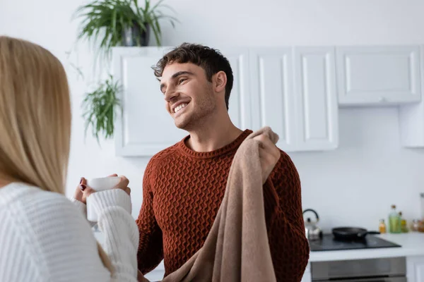 Позитивний чоловік тримає ковдру біля дівчини в светрі з чашкою чаю — стокове фото