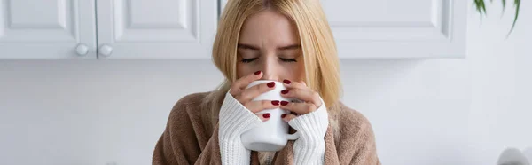 Young blonde woman in sweater and blanket drinking tea from cup, banner — Stock Photo