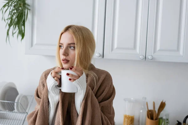 Jeune femme blonde en pull blanc et couverture tenant tasse de thé — Photo de stock