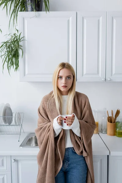 Jeune femme blonde en pull blanc et couverture tenant tasse de thé — Photo de stock