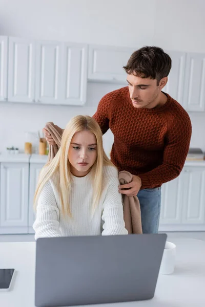 Fürsorglicher Freund im Pullover hält Decke neben Freundin, die von zu Hause aus am Laptop arbeitet — Stockfoto