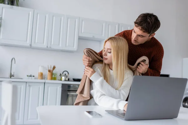 Premuroso fidanzato in maglione tenuta coperta vicino alla donna che lavora da casa vicino gadget — Foto stock